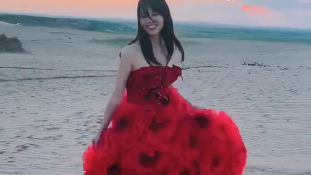 A girl in red dress walking on the sand