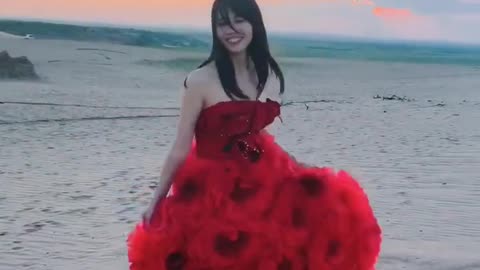 A girl in red dress walking on the sand