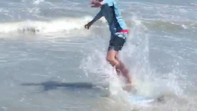 Kid blue shirt runs onto blue boogie board on beach falls into water