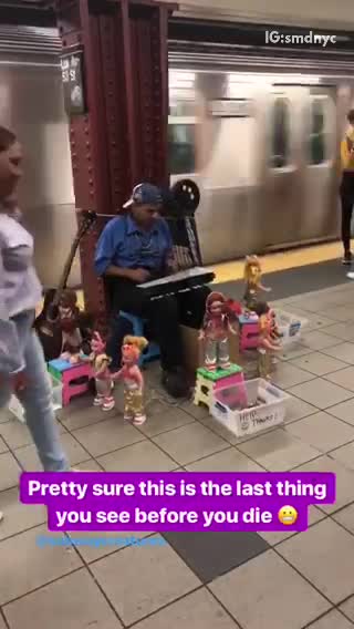 Guy blue shirt playing xylophone with a bunch of dancing dolls around him