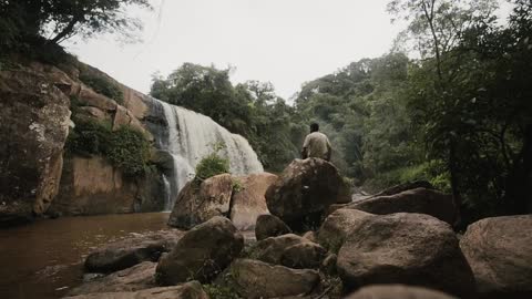 Man Sitting On Top Of Rock While Observes Waterfall