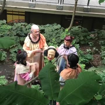 Four people in the forest doing prayers around decapitated head sculpture with headphones