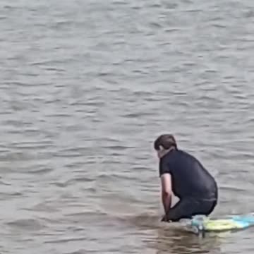 A guy struggling to get on a blue boogie board
