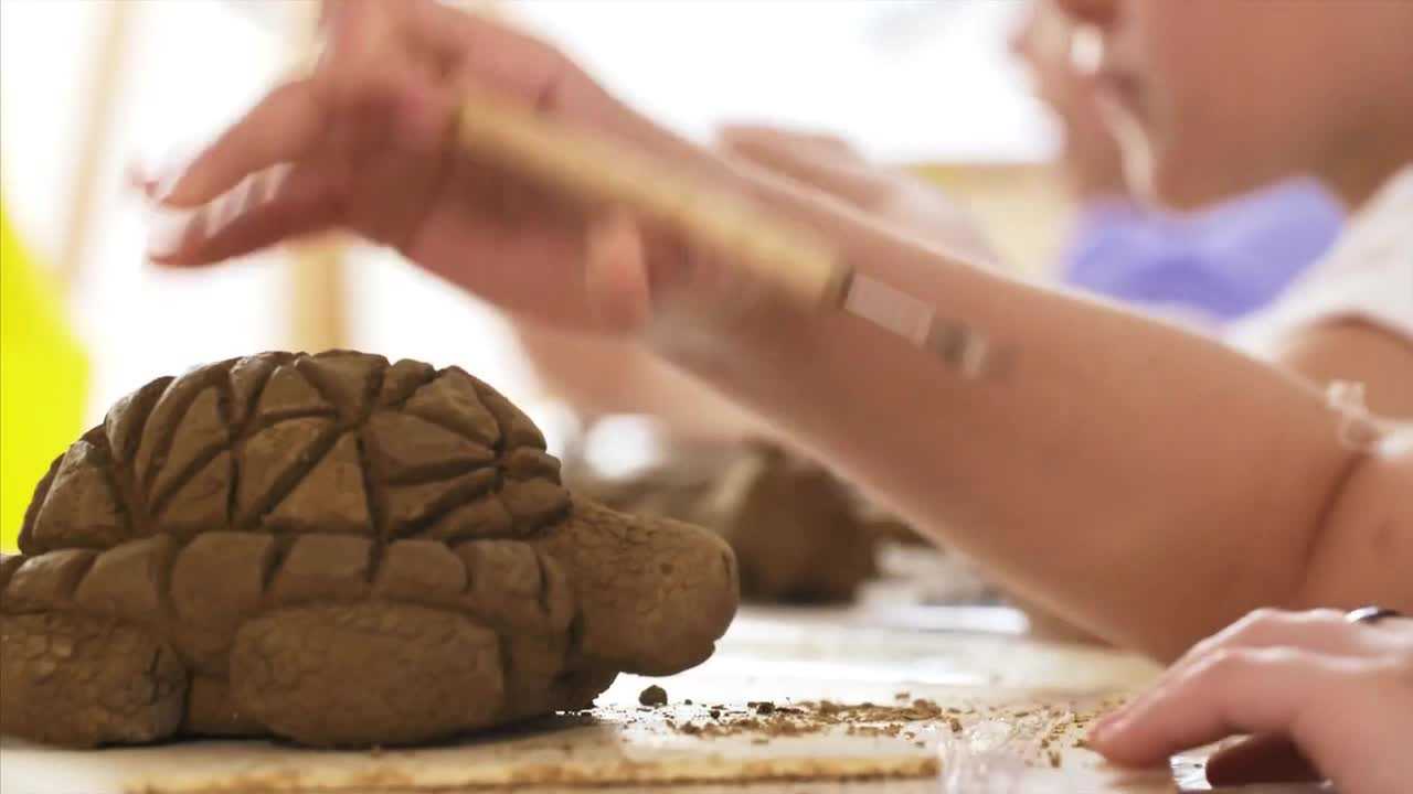 Child is scratching the texture of the scales on handmade turtle toy from clay