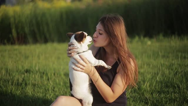 A girl and a dog are kissing in nature She carry on a dog