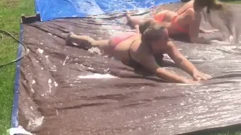 Two girls run into girl in orange bikini slip and slide