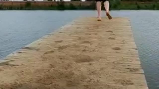 Guy red shirt runs on wooden dock to end and falls in to water lake