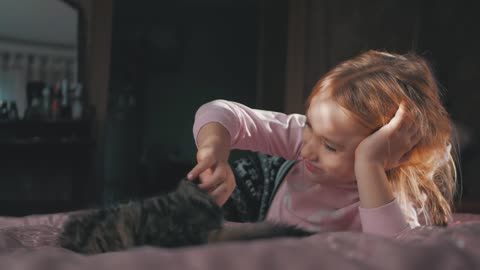 Little cute girl playing with kitten on bed at home