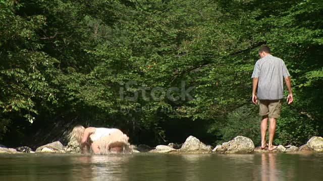 Couple is crossing the creek, when the girl slips and falls into the water.