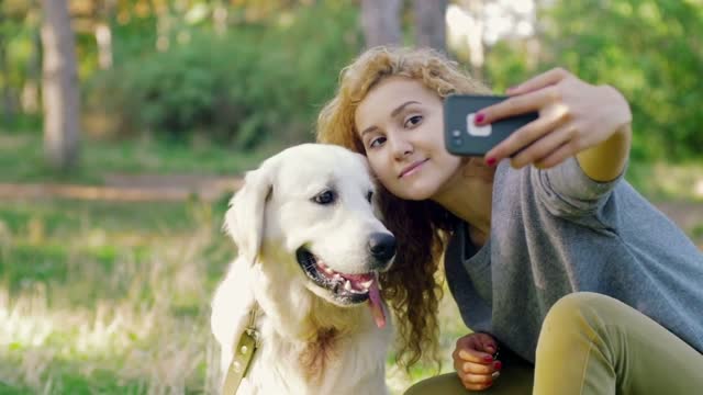 Young female doing selfie with labrador retriever dog in park