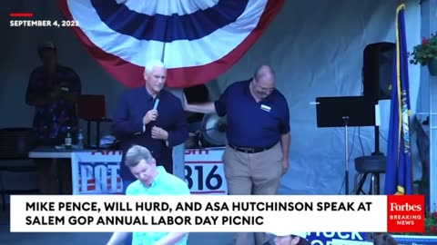 A man heckles Mike Pence and holds up a shirt featuring Trump's mugshot