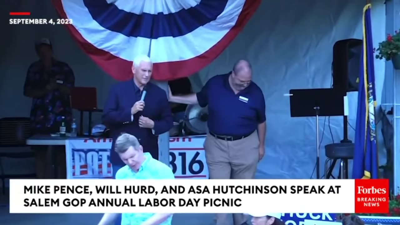A man heckles Mike Pence and holds up a shirt featuring Trump's mugshot