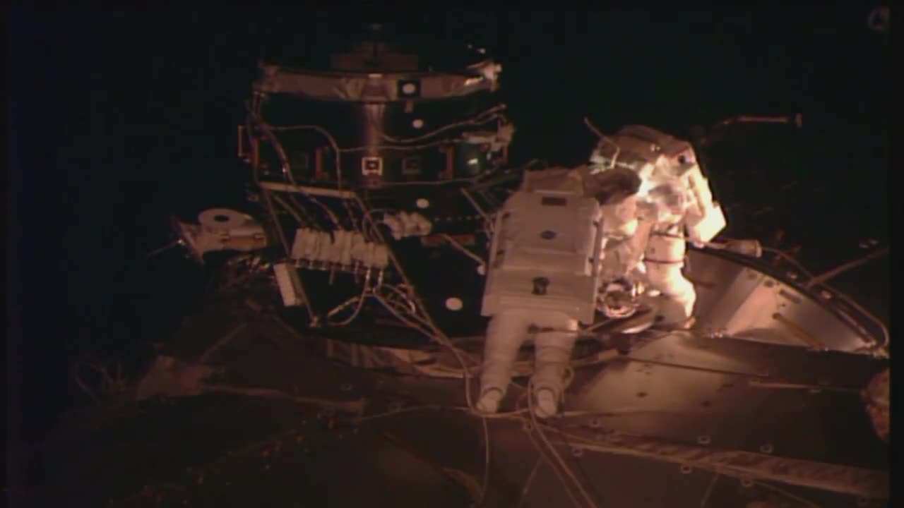 Space Station Crew Members Walk In Space to Connect Docking Adapter Component