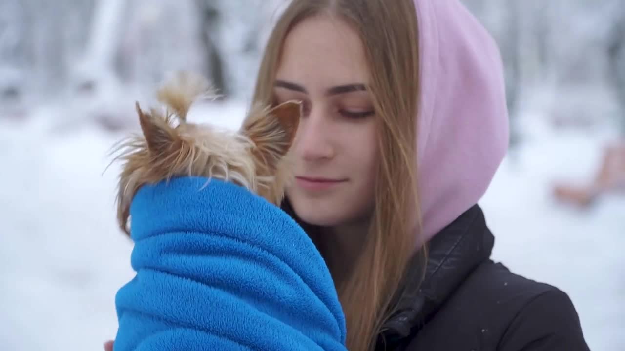 girl kissing a dog in a winter snow covered park holding a dog wrapped in a blue blanket