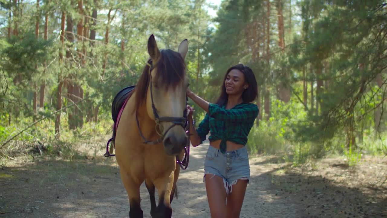 Affectionate cheerful african horsewoman in casual clothes holding