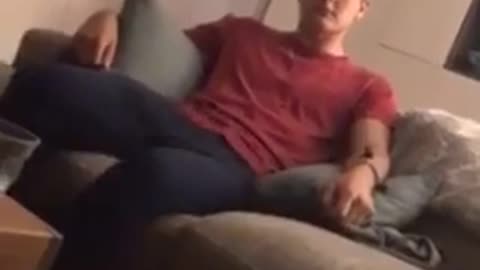 Guy sitting on couch in red shirt and dark blue pants wiggling legs