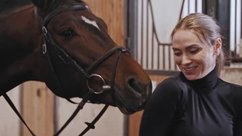 Smiling horsewoman puts on a plastic helmet standing near the horse