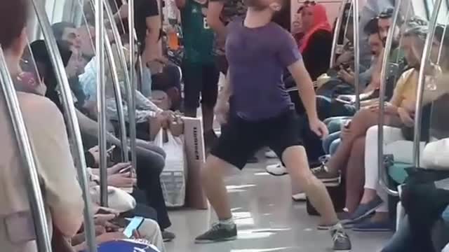 Guy black shorts purple shirt balancing soccer ball on subway train