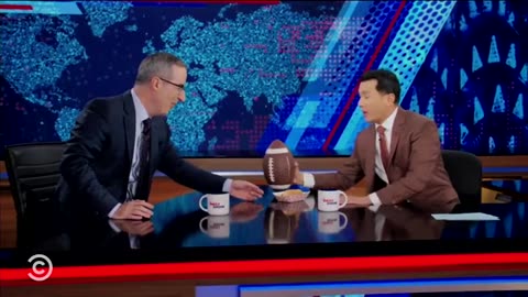John Oliver Eats a Hot Dog and Throws a Football on Air as a Challenge ‘to Be an American for