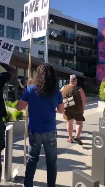 At today’s Dave Chappelle's Netflix special walkout rally, people chanting "trans lives matter” are going up against Chappelle supporters chanting “We like jokes"
