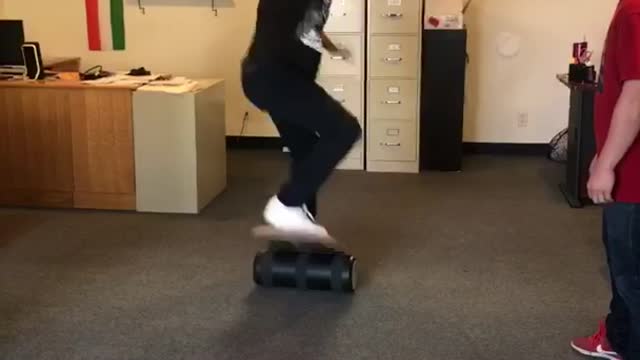 Black hat guy on balance board in office falls on shoulder