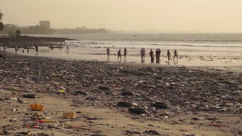 Young Men Playing Football In A Filthy Beach