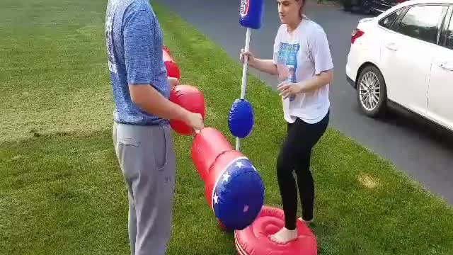 Girl and guy fighting on red and blue inflatable platforms fighting with blow up baton sticks