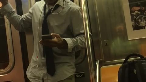 A man in a collard shirt and glasses dances on a subway train