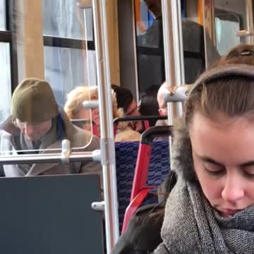 Couple making out on train behind lady with puffy blonde brown hair