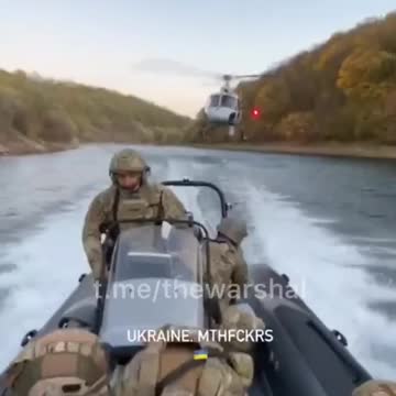 Ukrainian troops on a boat, running down river with a helicopter following directly behind them
