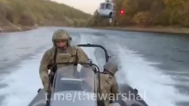 Ukrainian troops on a boat, running down river with a helicopter following directly behind them