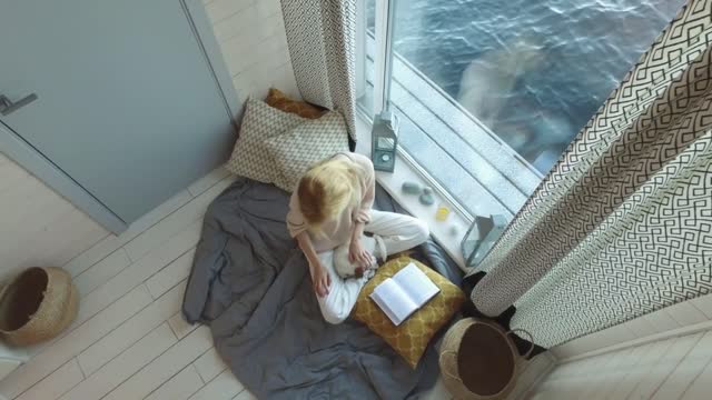 young woman stroke a puppy sitting by the window overlooking the water