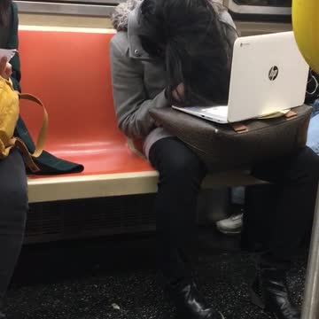 Woman slouches her head and falls asleep on a subway train with her laptop on her lap