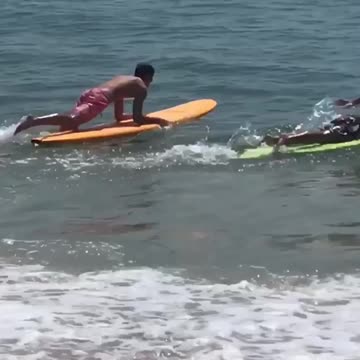 Guy orange surfboard rides wave into guy on green surfboard