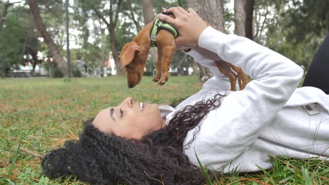 Girl lying on the grass holding her little dog on top.