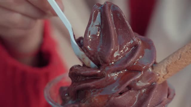 A girl tasting chocolate ice cream with a plastic spoon