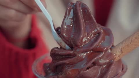 A girl tasting chocolate ice cream with a plastic spoon