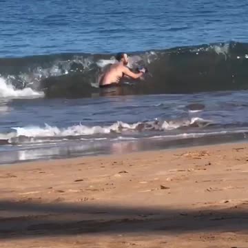 Man trying to take photo in water at beach gets knocked over by wave