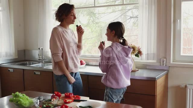 Happy teenage daughter and mom enjoying singing and cooking