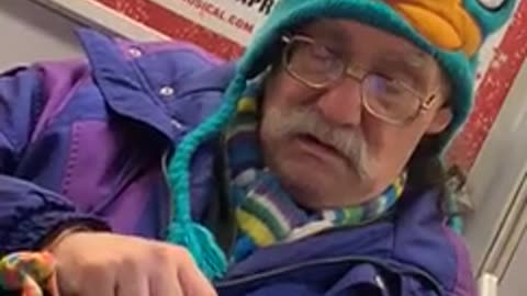 Old man wears perry the platypus beanie and bright purple jacket on subway train