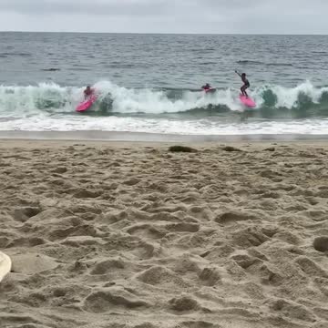 Three surfers pink surfboards fall off get knocked out by wave beach sand water