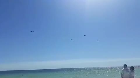 10 helicopters fly by in Florida off of beach.
