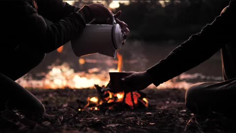 People pouring a warm drink around a campfire