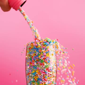Filling a glass cup with small sweets on a pink background