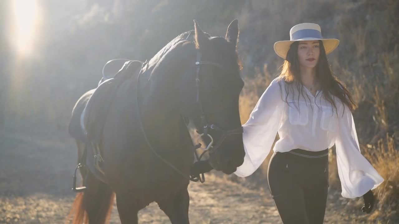 Young slim woman in white shirt and straw hat walking in slow motion holding horse bridle