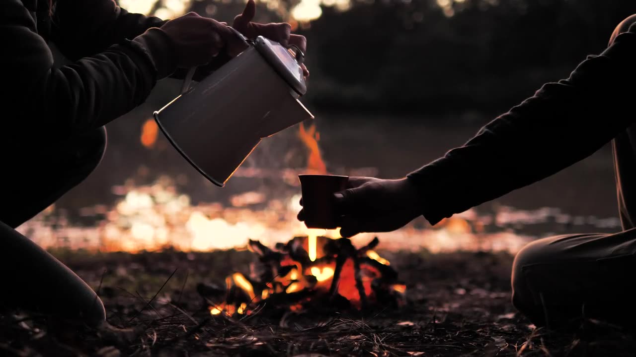 People pouring a warm drink around a campfire