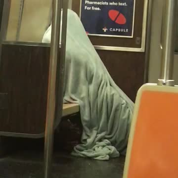 Person entirely covered from head to toe in gray blanket on subway train