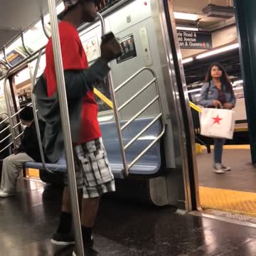 Man in red and flannel shorts dances on subway