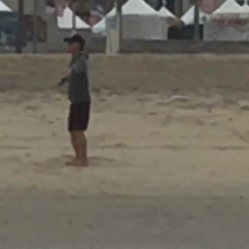 Guy black hat grey sweater arms out spinning in circles on beach sand