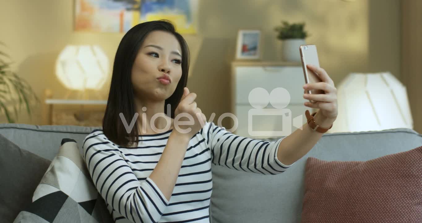 Young Woman In Striped Shirt Posing To The Smartphone Camera And Smiling While Taking A Selfie Photo